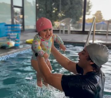 Un adulto sostiene a un bebé con gorro dentro de la piscina temperada